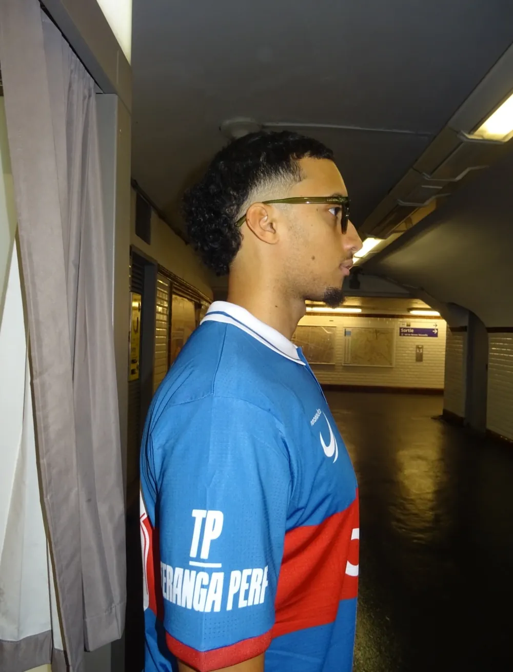 AS Xenon player in profile wearing a blue and red football jersey with a white polo collar and a printed sleeve sponsor, showing the fine textured polyester knit